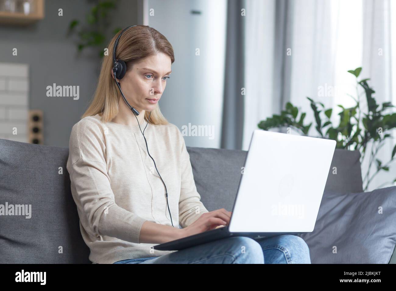 Die Frau arbeitet zu Hause als Online-Consultant, nutzt ein Headset und einen Laptop für einen Videoanruf Stockfoto