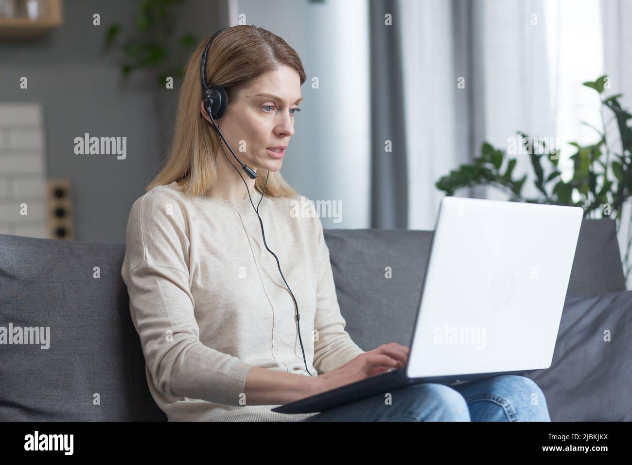 Die Frau arbeitet zu Hause als Online-Consultant, nutzt ein Headset und einen Laptop für einen Videoanruf Stockfoto