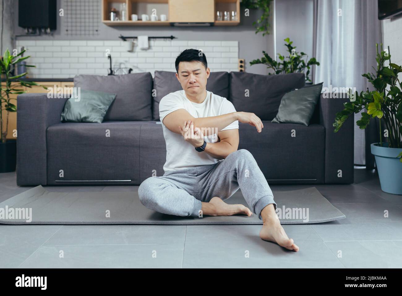 Der Mann wurde verletzt, während er zu Hause Fitness machte, der Asian schmerzte seine Schulter, seine Armmuskeln Stockfoto
