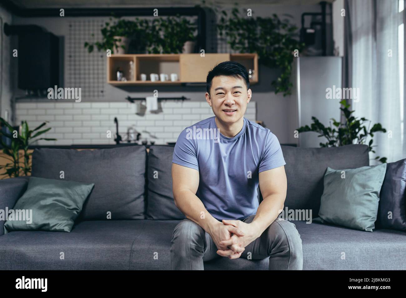 Porträt eines Mannes zu Hause, Asian selbst lächelnd und die Kamera auf der Couch sitzend anblickend Stockfoto