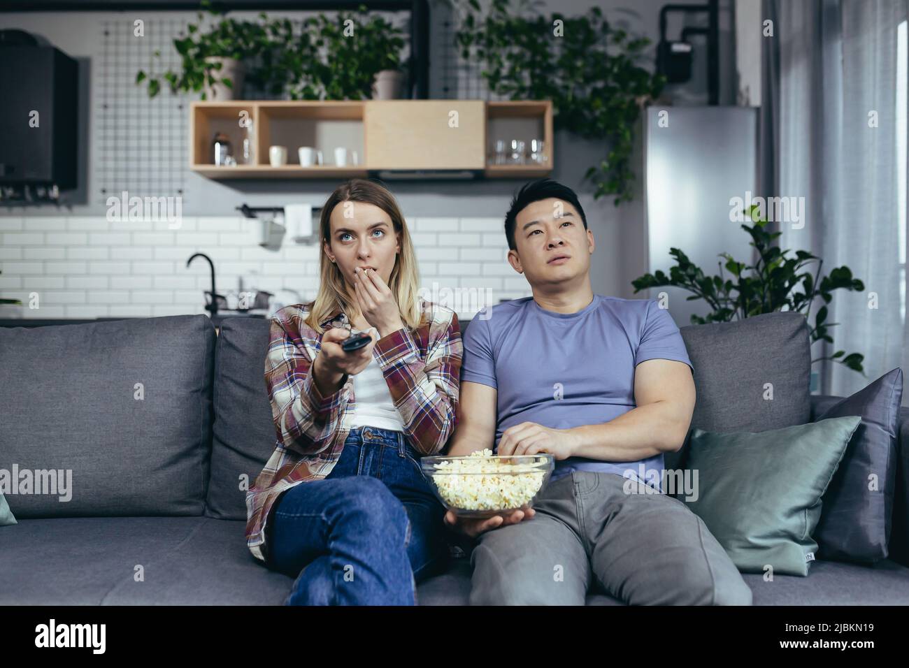 Ehepaar, Mann und Frau zu Hause, die zusammen Fernsehen, gelangweilt, die Kanäle zu wechseln, einen interessanten Sender zu finden, Familie, die zu Hause auf dem Sofa sitzt Stockfoto