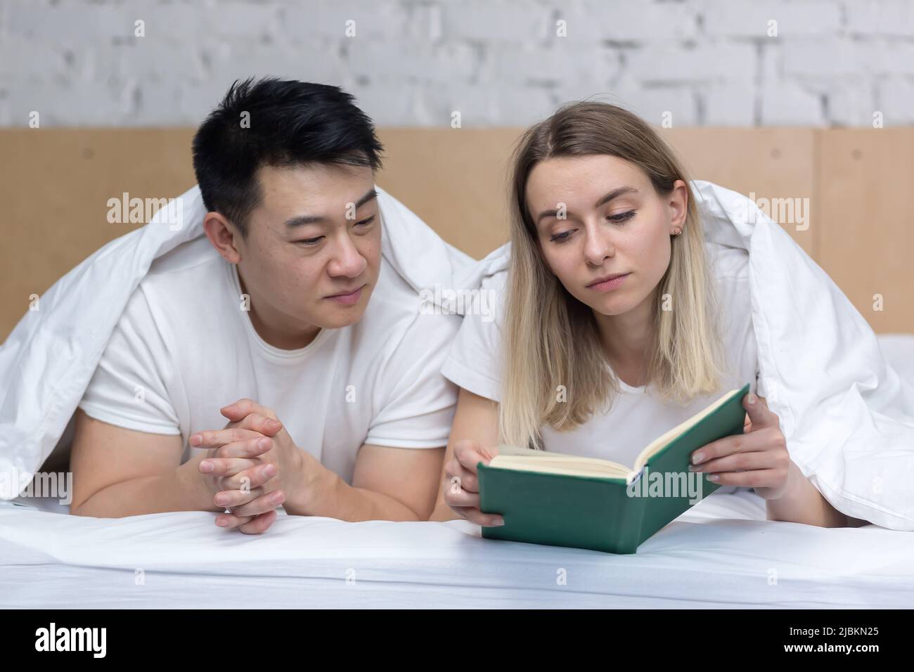 Glückliches asiatisches Paar in Liebe und Frau liegen zusammen im Bett und lesen ein Buch Stockfoto