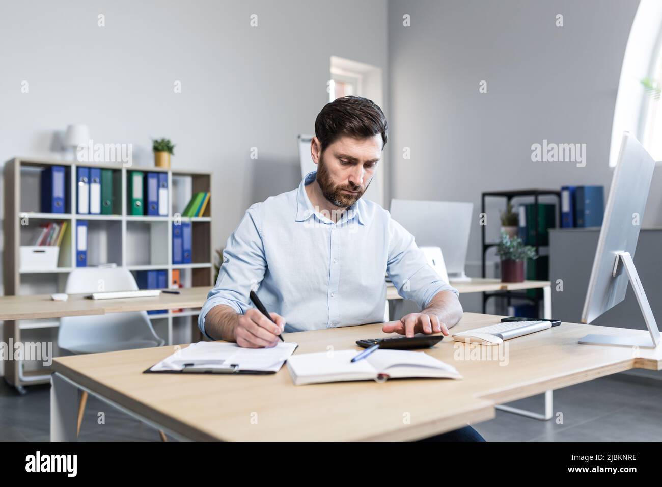 Porträt eines jungen Mannes. Buchhalter, Ökonom, Finanzierer. Setzt auf einen Rechner, sitzt am Schreibtisch am Computer, arbeitet mit Dokumenten Stockfoto