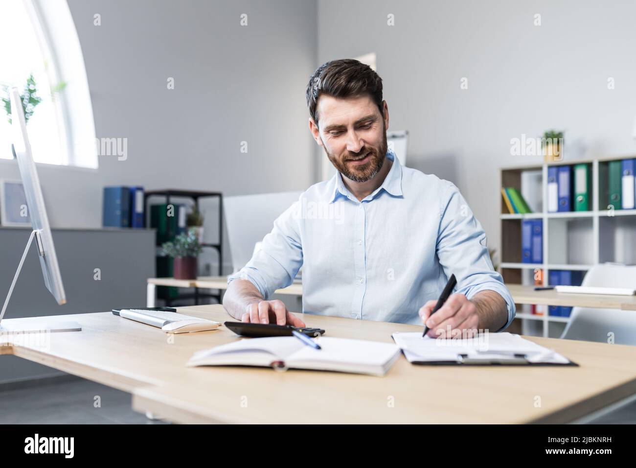 Porträt eines jungen Mannes. Buchhalter, Ökonom, Finanzierer. Setzt auf einen Rechner, sitzt am Schreibtisch am Computer, arbeitet mit Dokumenten Stockfoto