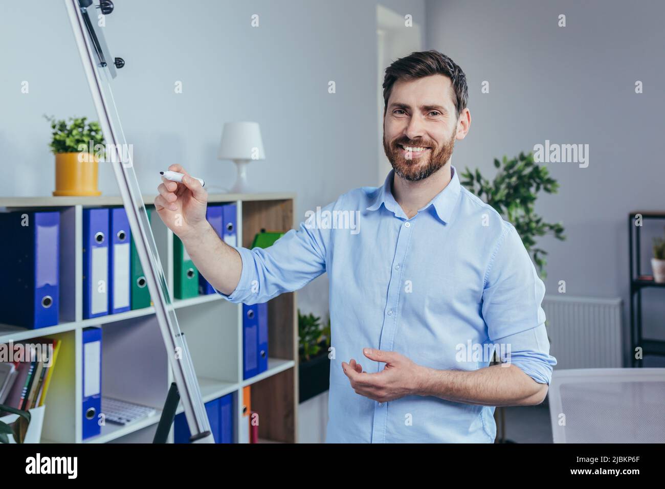 Porträt eines erfolgreichen Unternehmensgründers, ein Mann schaut auf die Kamera und lächelt auf ein Whiteboard für Notizen, hält ein Tablet, beschreibt eine Business str Stockfoto