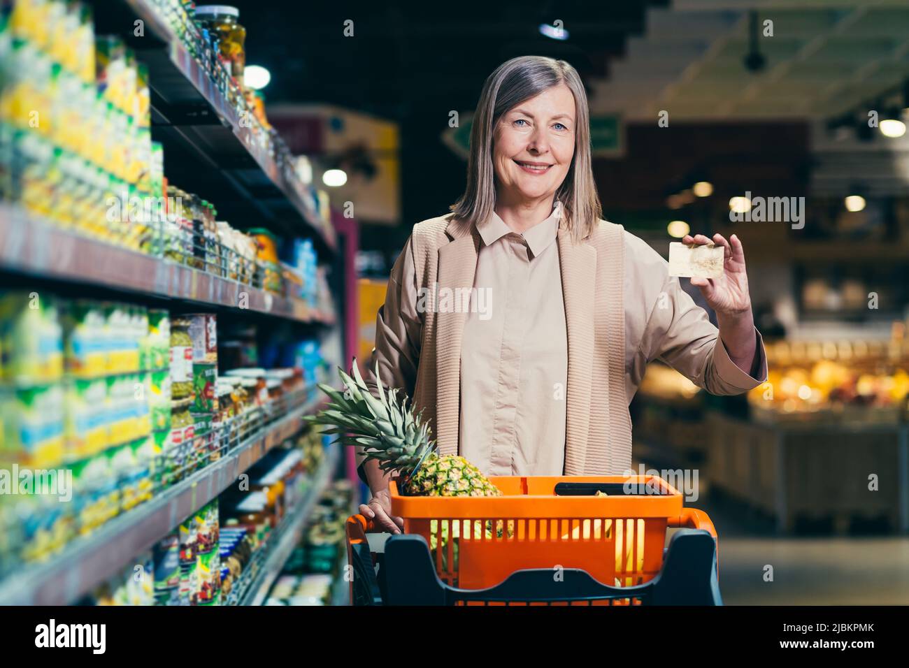 Porträt einer schönen älteren Frau in einem Geschäft, Supermarkt, mit einer Kreditkarte in den Händen. Steht zwischen den Regalen eines Ladens, Supermarkt w Stockfoto
