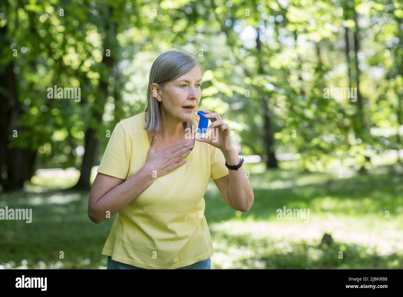 Saisonale Allergien. Eine ältere Frau im Park hat in der Natur Atembeschwerden, nutzt einen Inhalator. Niest und hustet in ein Taschentuch. Hat alle Stockfoto
