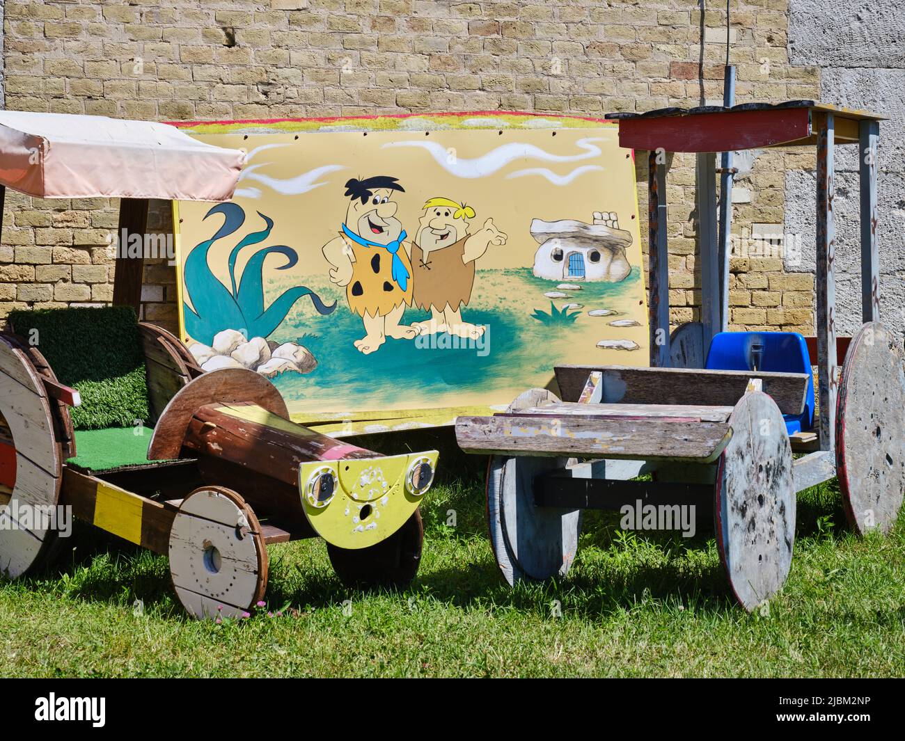 Holzautos und Cartoongemälde im Freien neben einer Steinmauer. Stockfoto