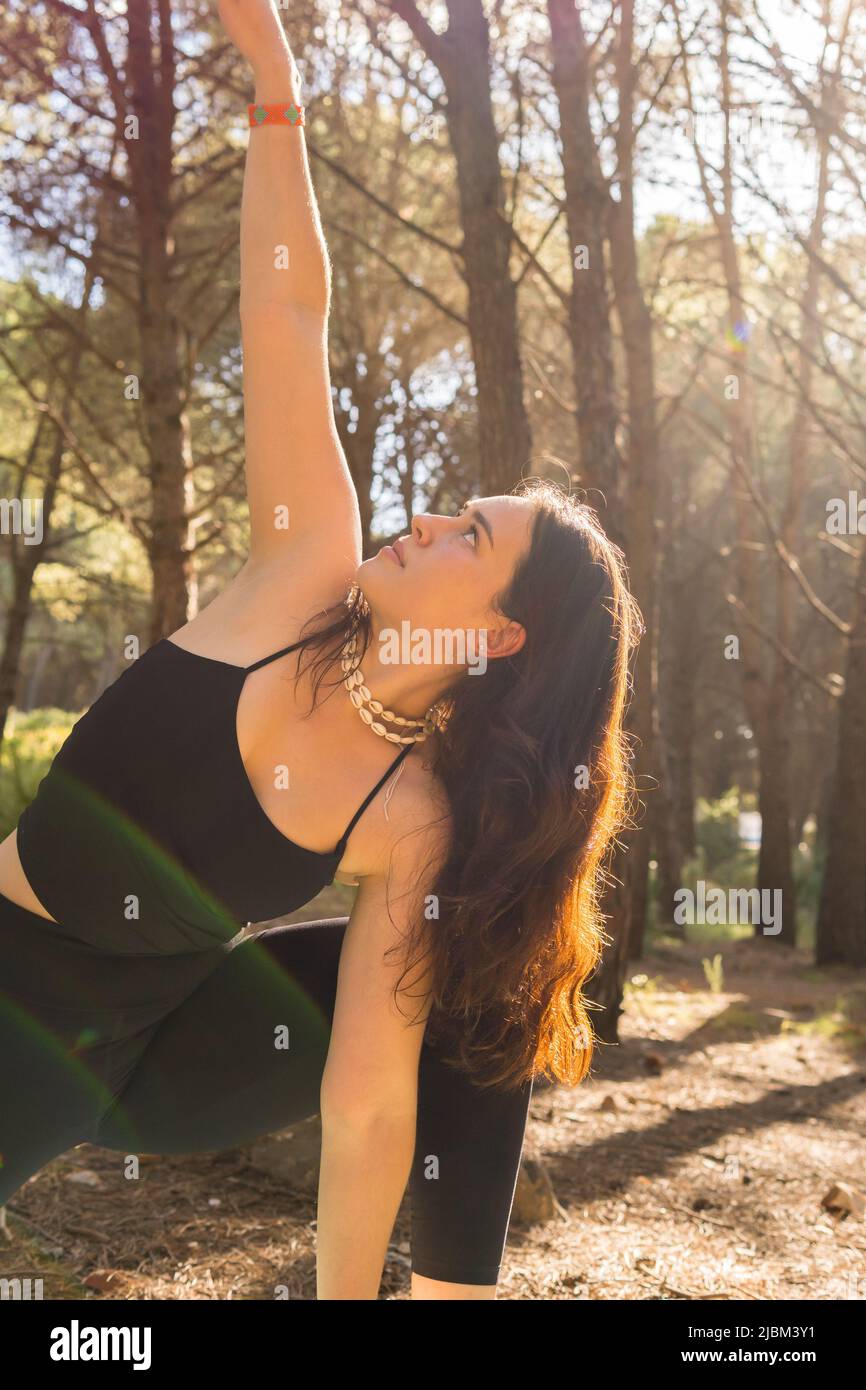 Junge schöne Mädchen tun Yoga-Positionen bei Sonnenuntergang in einem Wald von Bäumen umgeben entspannen. Vertikales Foto, Nahaufnahme Stockfoto