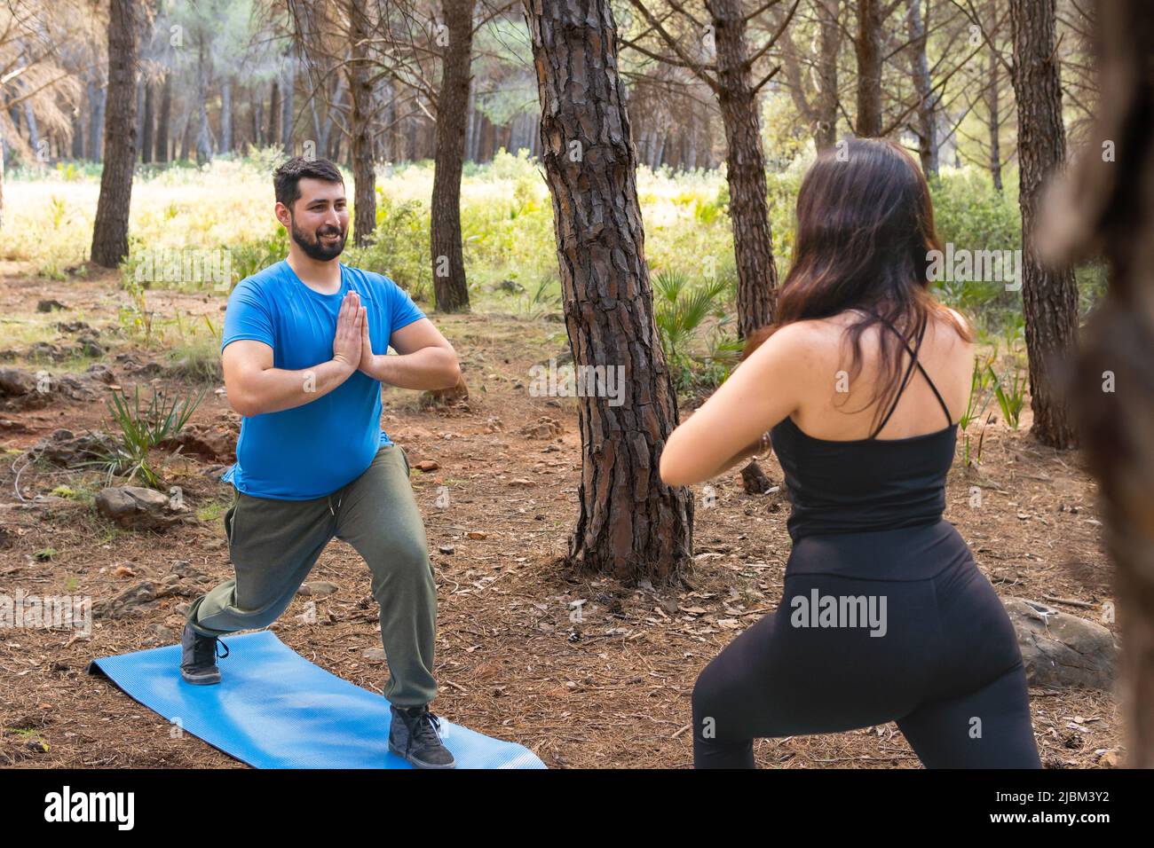 Junge Menschen üben Yoga in einem Wald mit ihrer blauen Matte an einem sonnigen Tag zur Entspannung. Stockfoto