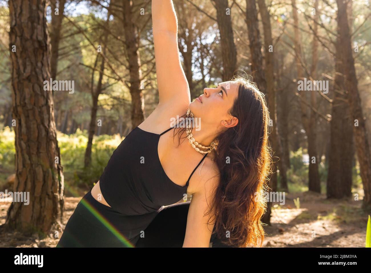 Junge schöne Mädchen tun Yoga-Positionen bei Sonnenuntergang in einem Wald von Bäumen umgeben entspannen. Horizontales Foto, mittlere Aufnahme Stockfoto