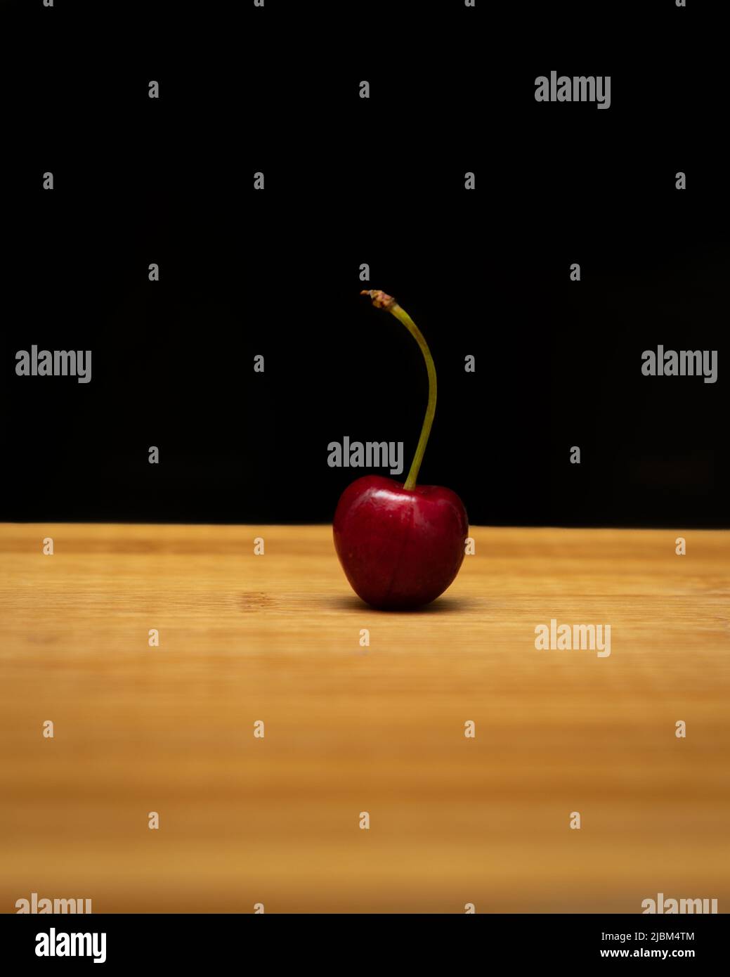 Single RIPE Cherry platziert auf einem Holzschneidebrett auf einem dunkelschwarzen Hintergrund. Stockfoto