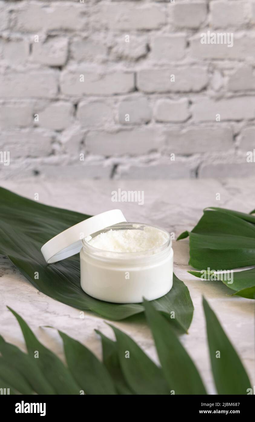 Geöffnetes weißes Glas und Monstera-Blätter auf Marmortisch aus nächster Nähe. Modell der Markenverpackung. Hautpflegeprodukt, Creme oder Butter. Hausgemachte Herba Stockfoto