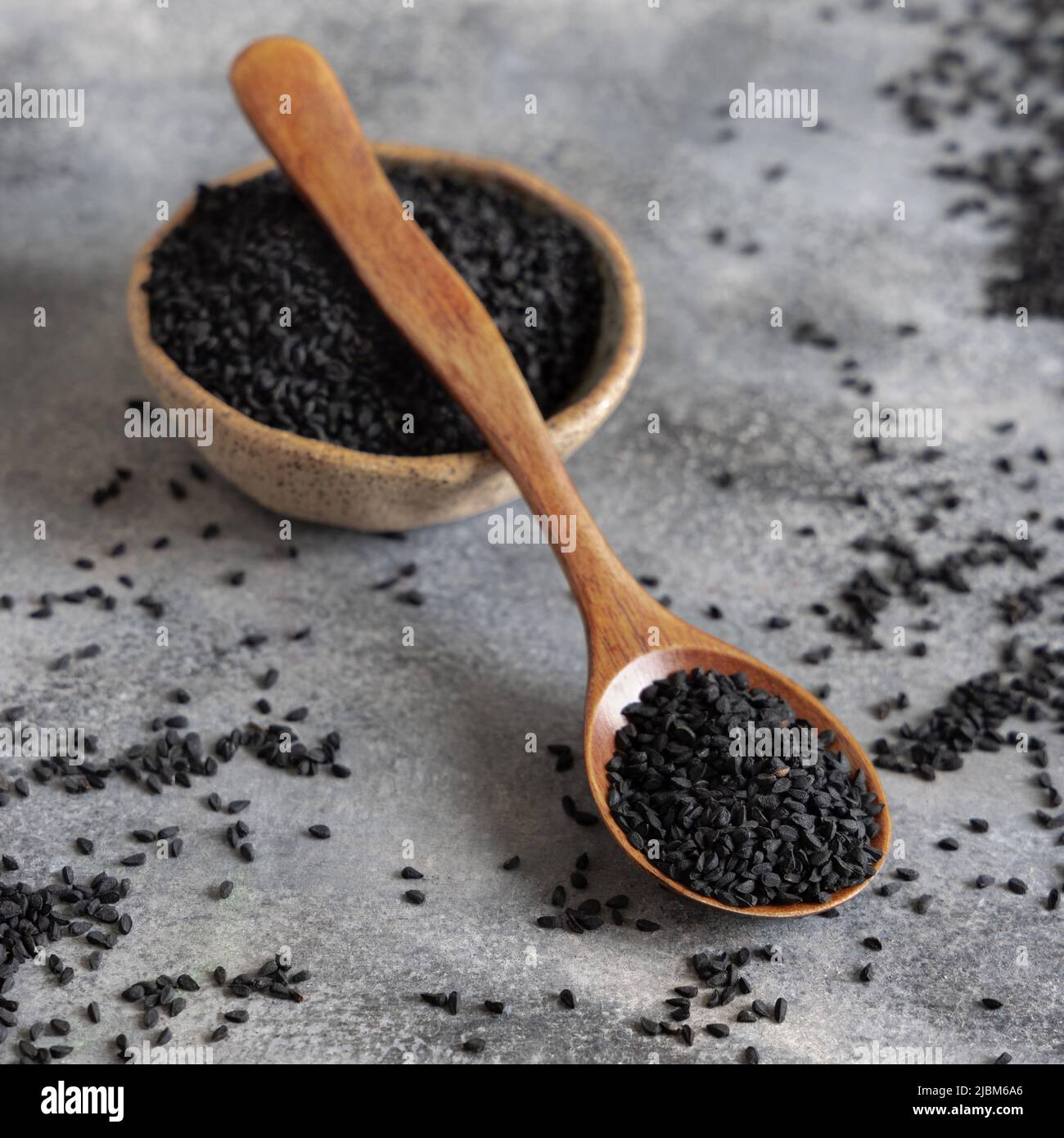 Schale mit indischem Gewürz Schwarzer Kreuzkümmel (Nigella sativa oder Kalonji) auf grauem Tisch mit einem Holzlöffel, Nahaufnahme mit Kopierraum. Traditionelle asiatische medi Stockfoto