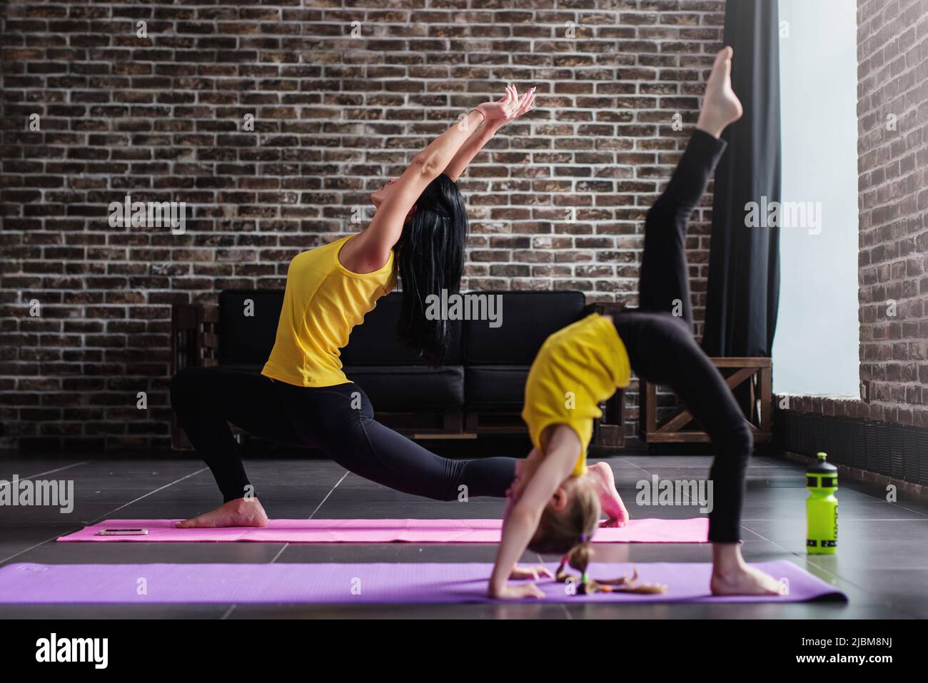 Junge Erwachsene mit Halbmond-Ausfallschritt und Kind mit einem Bein in umgekehrter Mitarbeiterposition während des Yoga-Trainings im stilvollen Loft-Studio Stockfoto