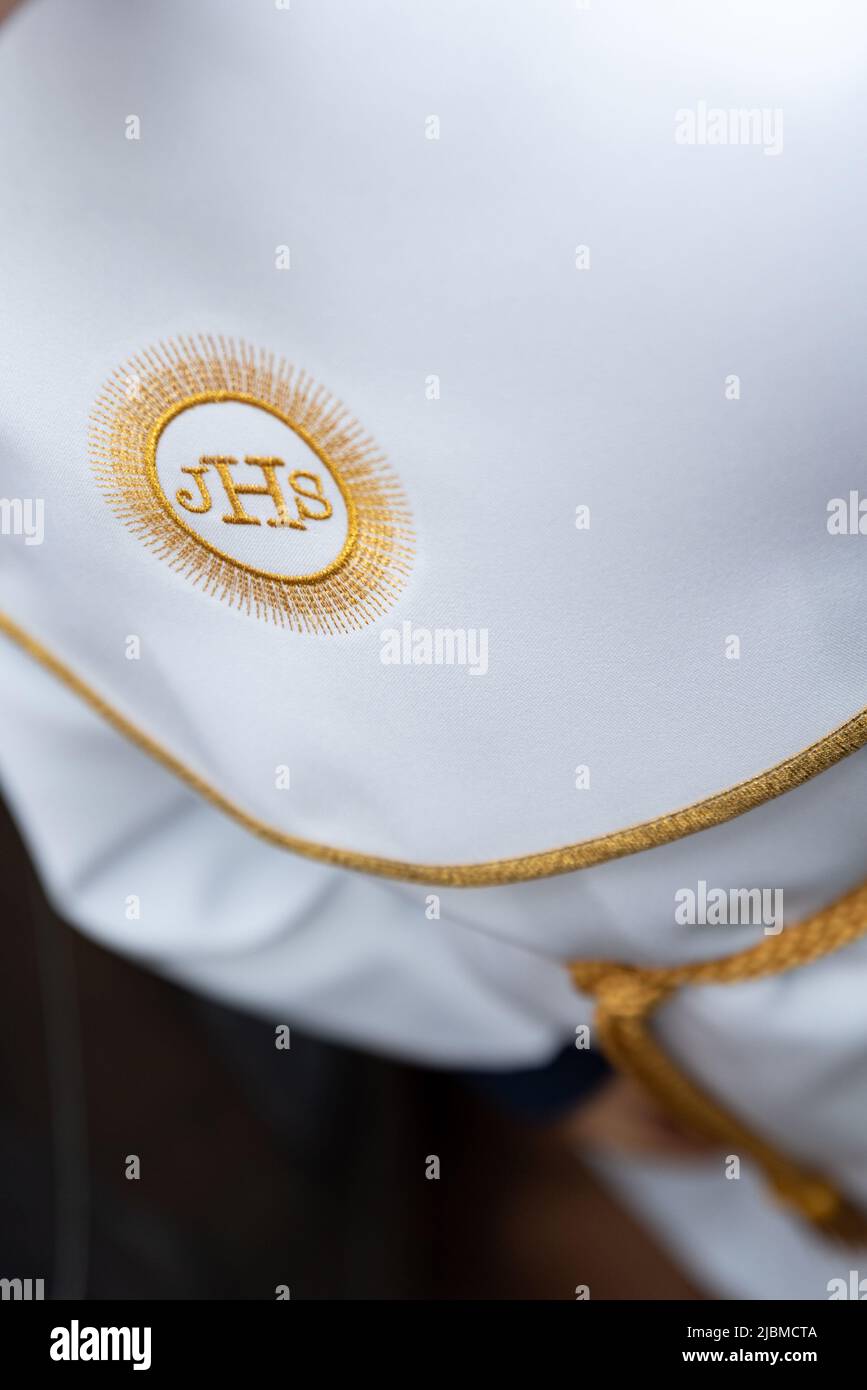 IHS christliches Symbol auf einem Kommunionskind. IHS Christogramm bestickt mit Goldfaden auf einer weißen Alba. Kleid der ersten Heiligen Kommunion. Stockfoto