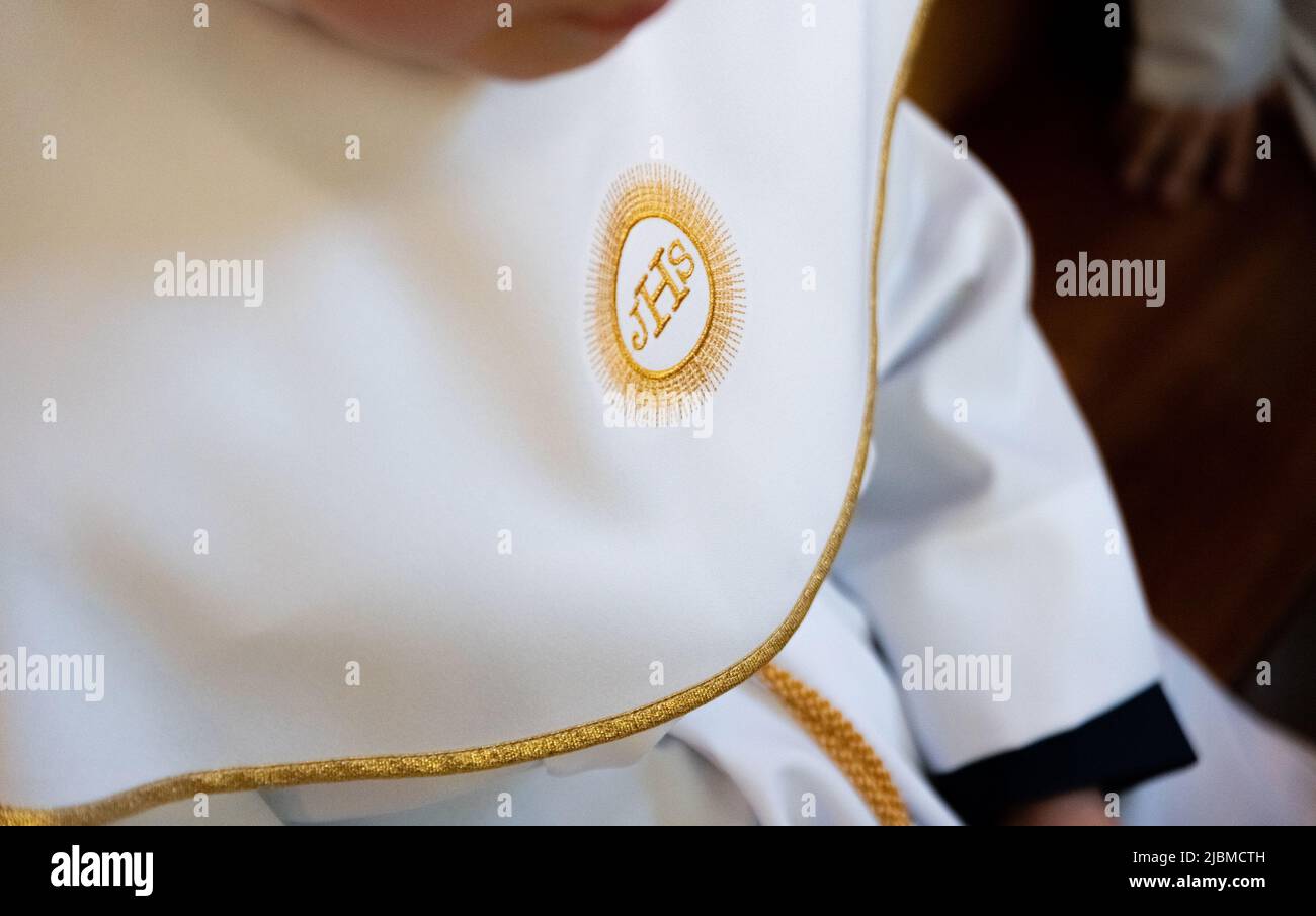 IHS christliches Symbol auf einem Kommunionskind. IHS Christogramm bestickt mit Goldfaden auf einer weißen Alba. Kleid der ersten Heiligen Kommunion. Stockfoto
