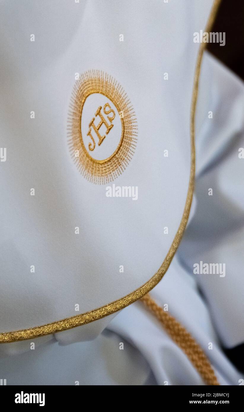 IHS christliches Symbol auf einem Kommunionskind. IHS Christogramm bestickt mit Goldfaden auf einer weißen Alba. Kleid der ersten Heiligen Kommunion. Stockfoto