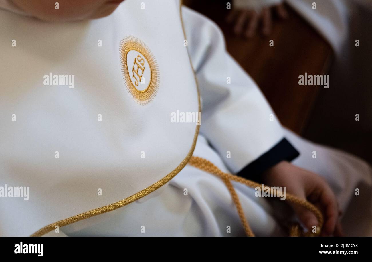IHS christliches Symbol auf einem Kommunionskind. IHS Christogramm bestickt mit Goldfaden auf einer weißen Alba. Kleid der ersten Heiligen Kommunion. Stockfoto