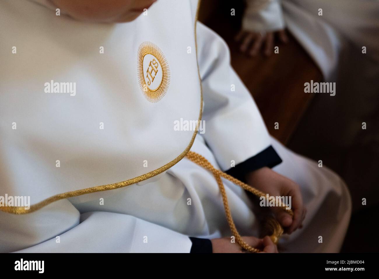 IHS christliches Symbol auf einem Kommunionskind. IHS Christogramm bestickt mit Goldfaden auf einer weißen Alba. Kleid der ersten Heiligen Kommunion. Stockfoto