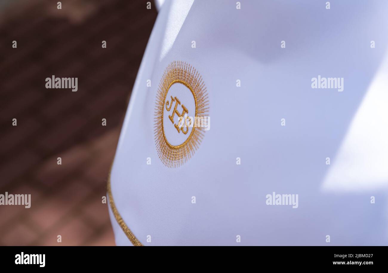 IHS christliches Symbol auf einem Kommunionskind. IHS Christogramm bestickt mit Goldfaden auf einer weißen Alba. Kleid der ersten Heiligen Kommunion. Stockfoto