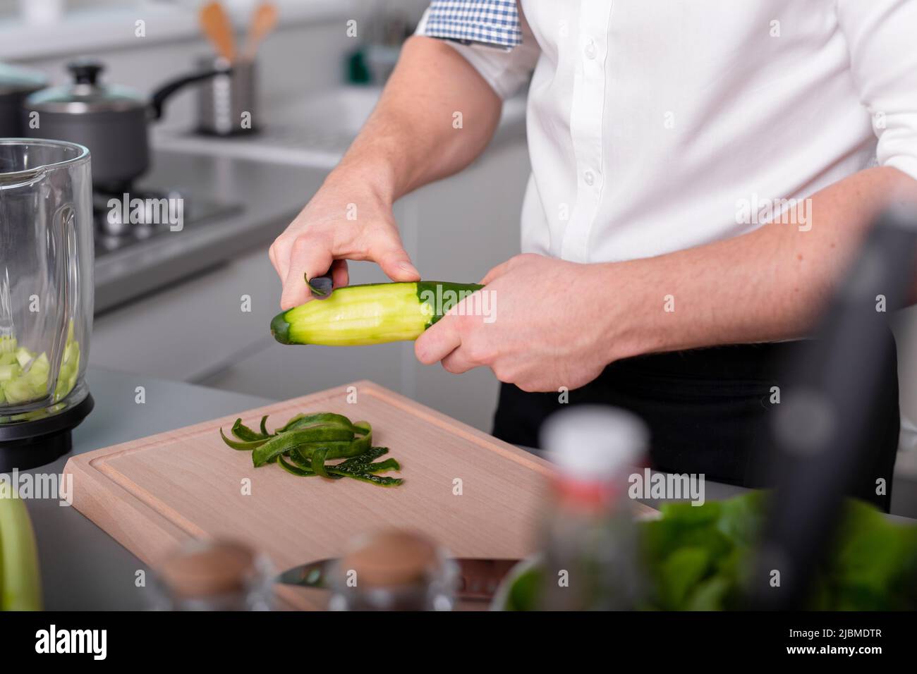 Mann bereitet vegetarisches Essen zu Essen Schälende Gurke auf Schneidebrett. Hausgemachte Mahlzeit Stockfoto