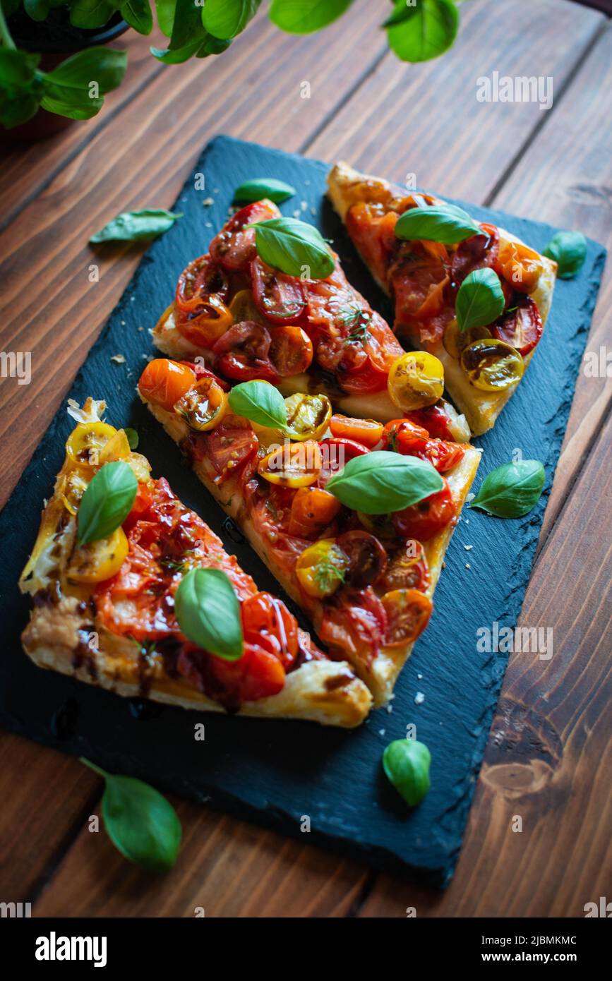 Tomatenblätterteigkuchen mit Balsamico-Essig und frischem Basilikum auf Steinplatte Stockfoto