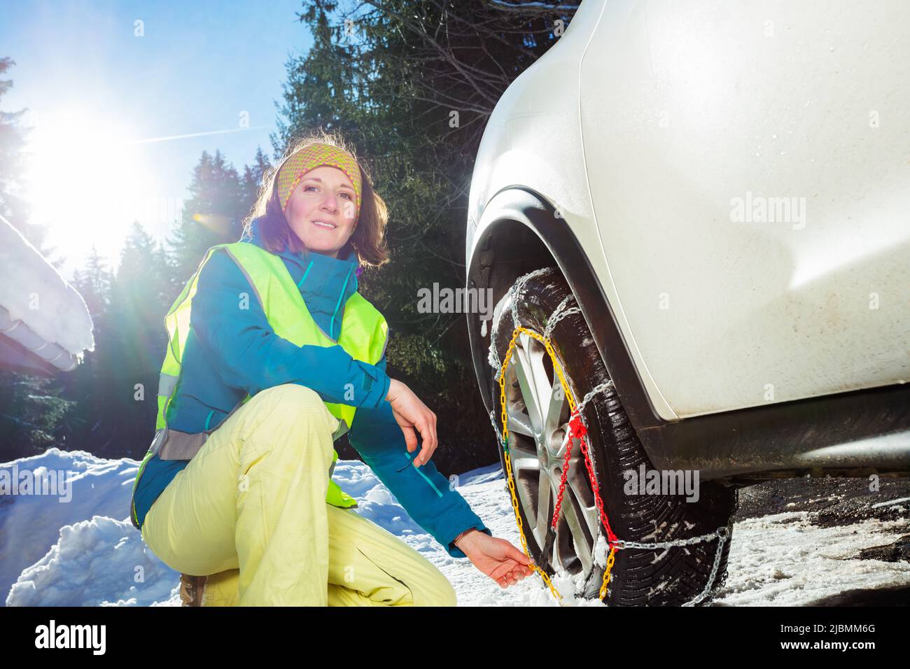 Frau legte Winterketten für Autorad auf verschneite Straße Stockfoto