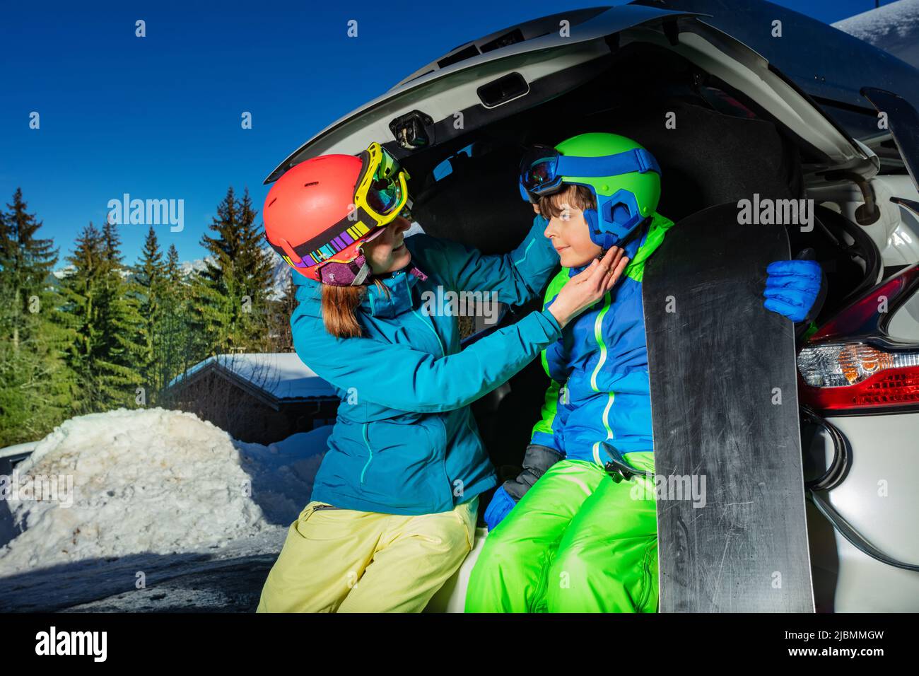 Mutter hilft Jungen, Skihelm im Kofferraum zu setzen Stockfoto