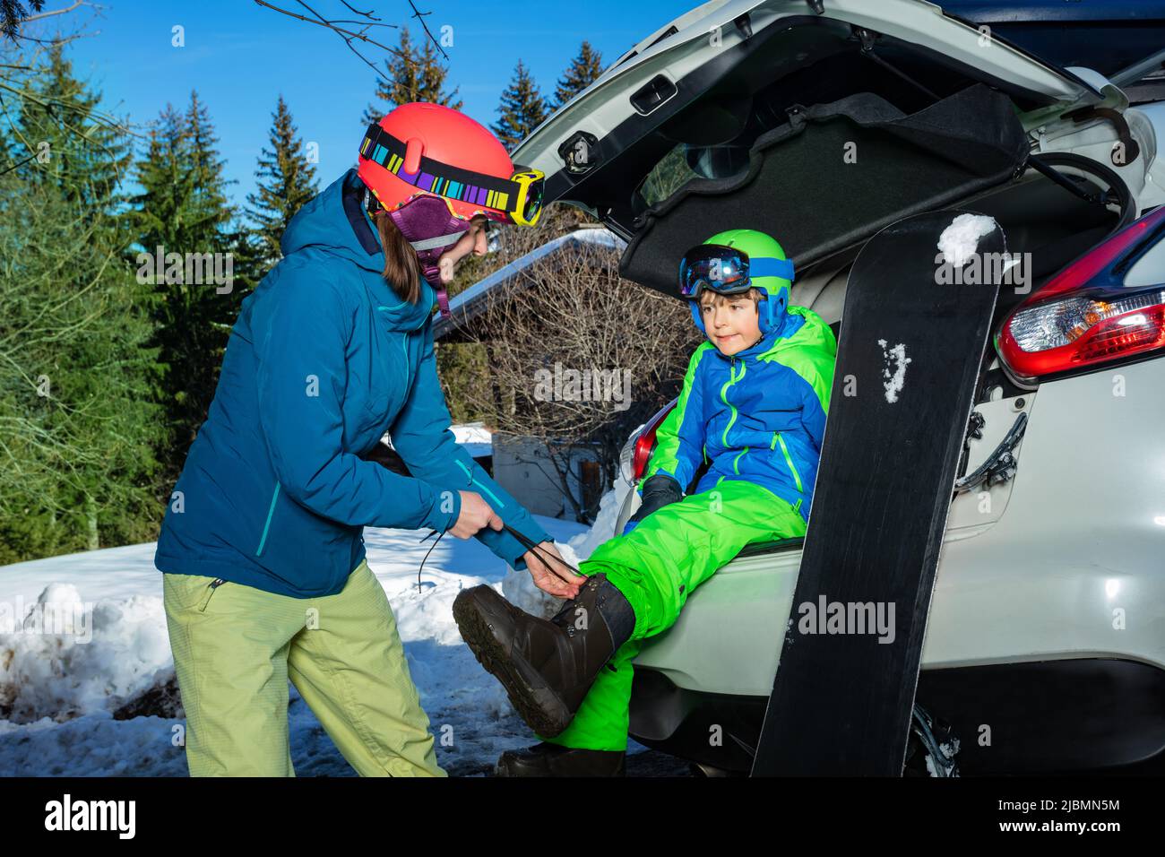 Mutter hilft dem Jungen, Snowboardschuhe auf dem Parkplatz anzuziehen Stockfoto