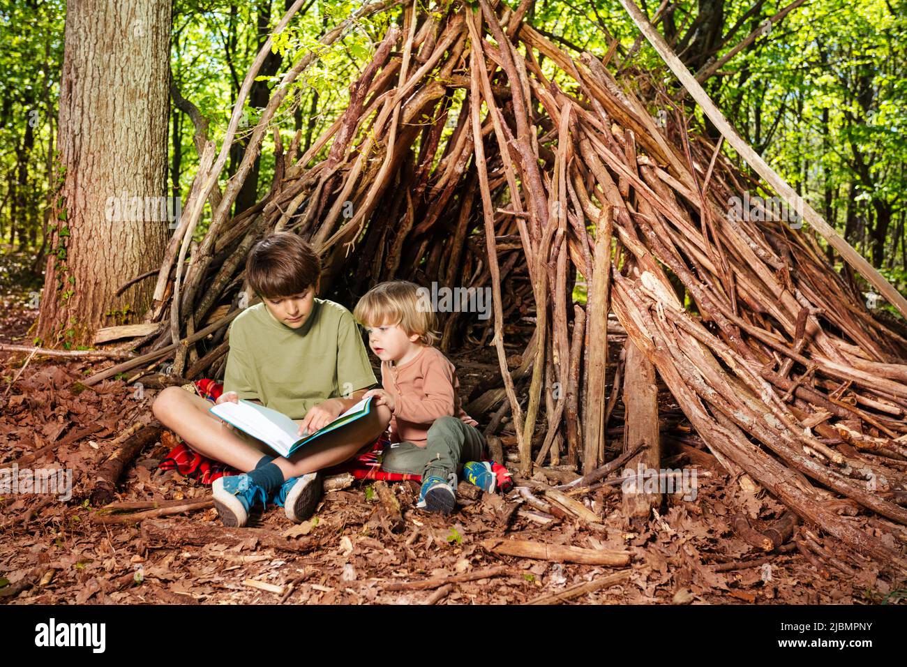 Zwei Kinder, Jungen lesen Buch, sitzen in der Hütte der Zweige Stockfoto