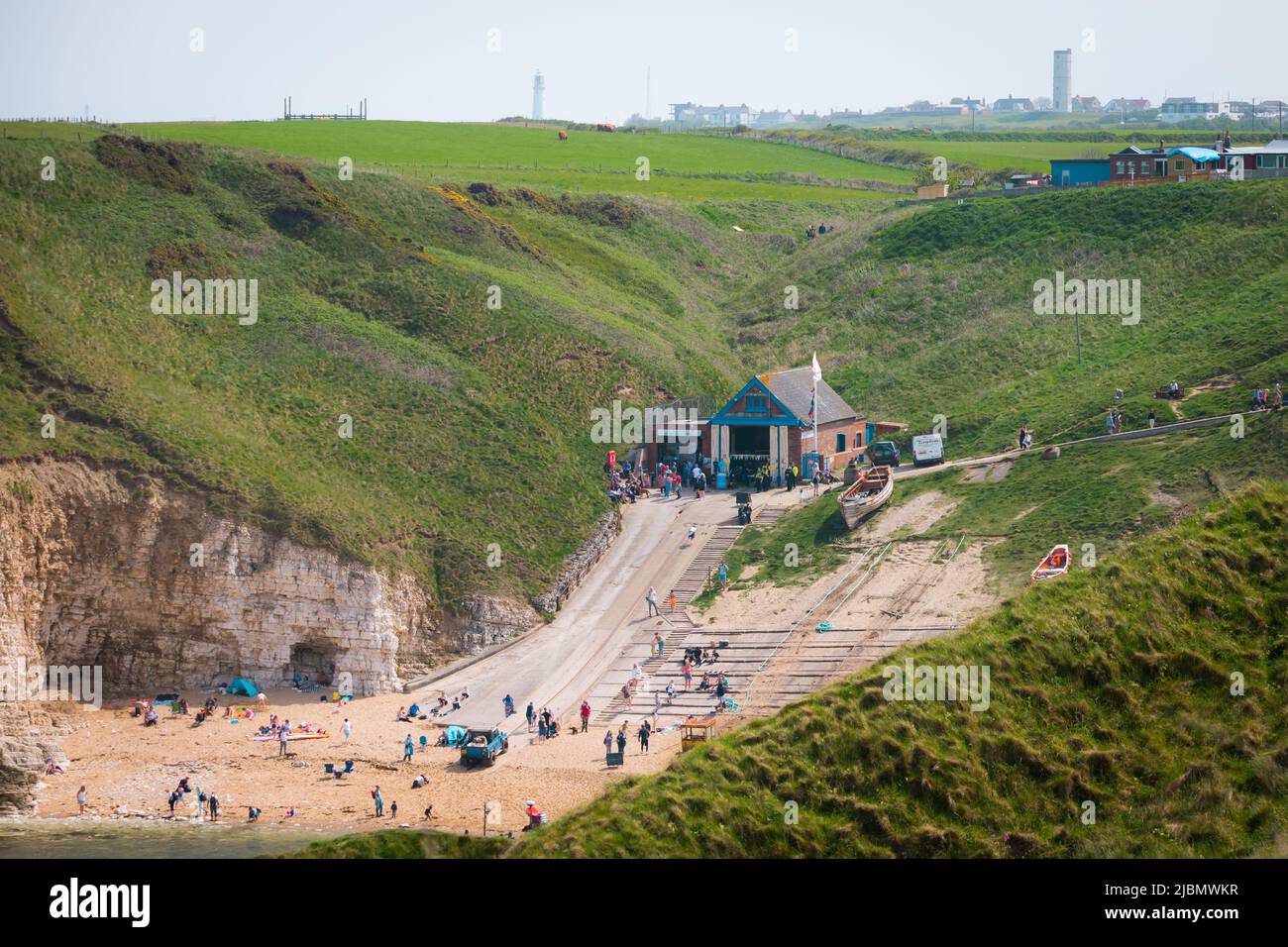 Weite Landschaft der Slipanlage, des Strandes und des RNLI-Rettungsboothauses in Flamborough North Landing an einem sonnigen Tag Stockfoto
