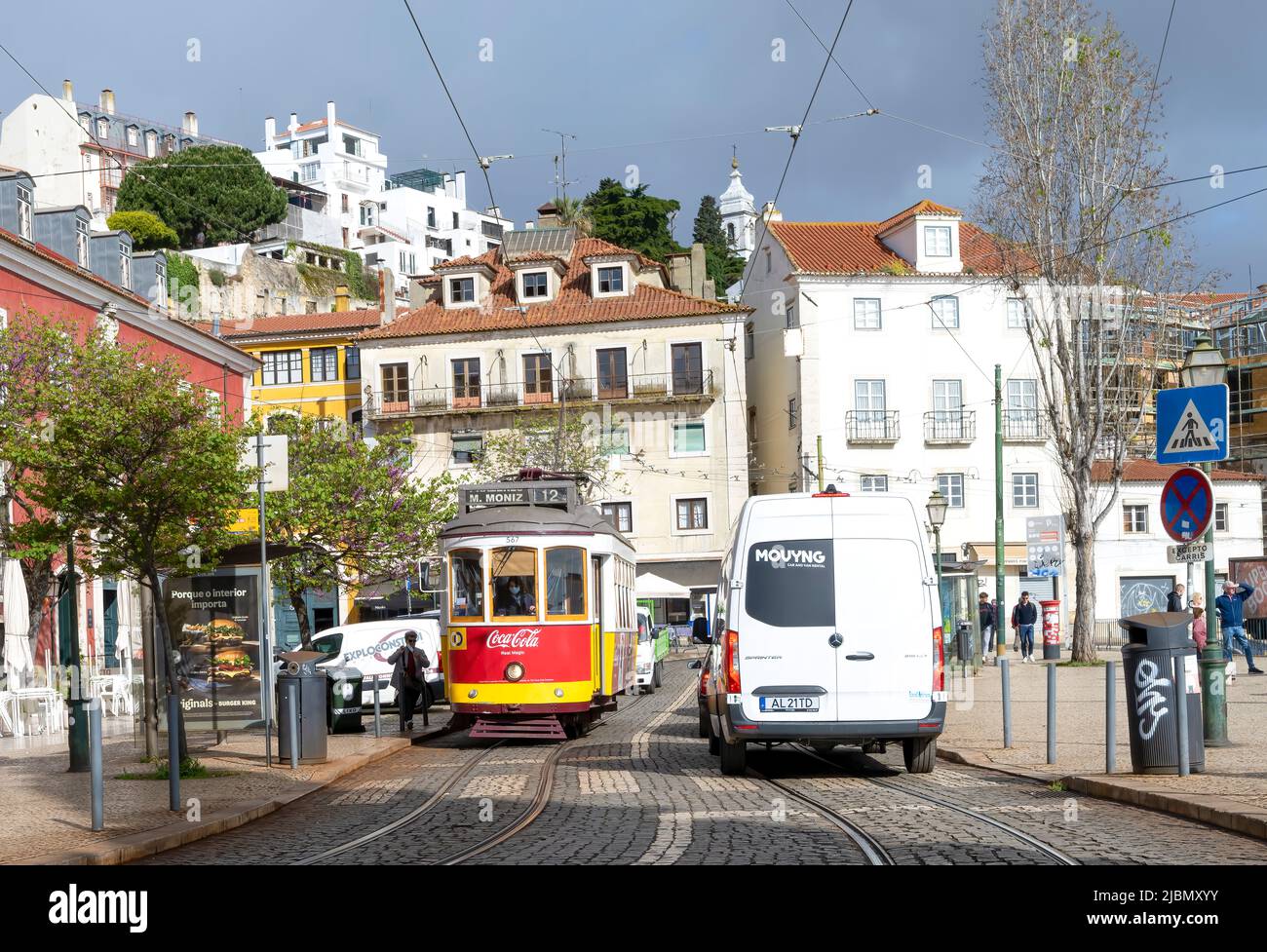 Ein weißer Lieferwagen fährt an einer roten Straßenbahn vorbei, die Passagiere im Zentrum von Lissabon, der Hauptstadt Portugals, abholt Stockfoto