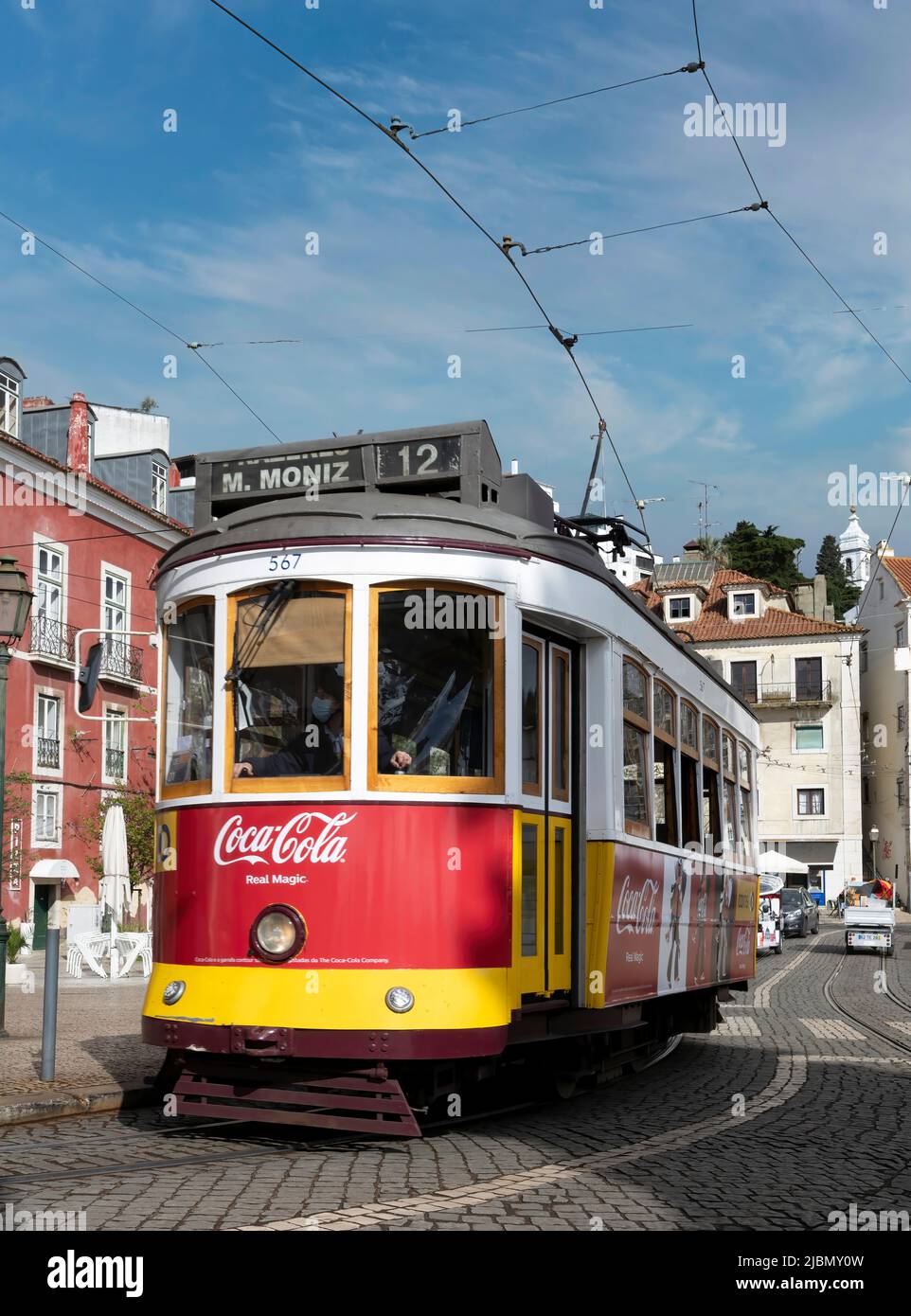 Eine traditionelle rote Straßenbahn fährt über die nassen, gepflasterten Straßen im Zentrum von Lissabon, der Hauptstadt Portugals Stockfoto