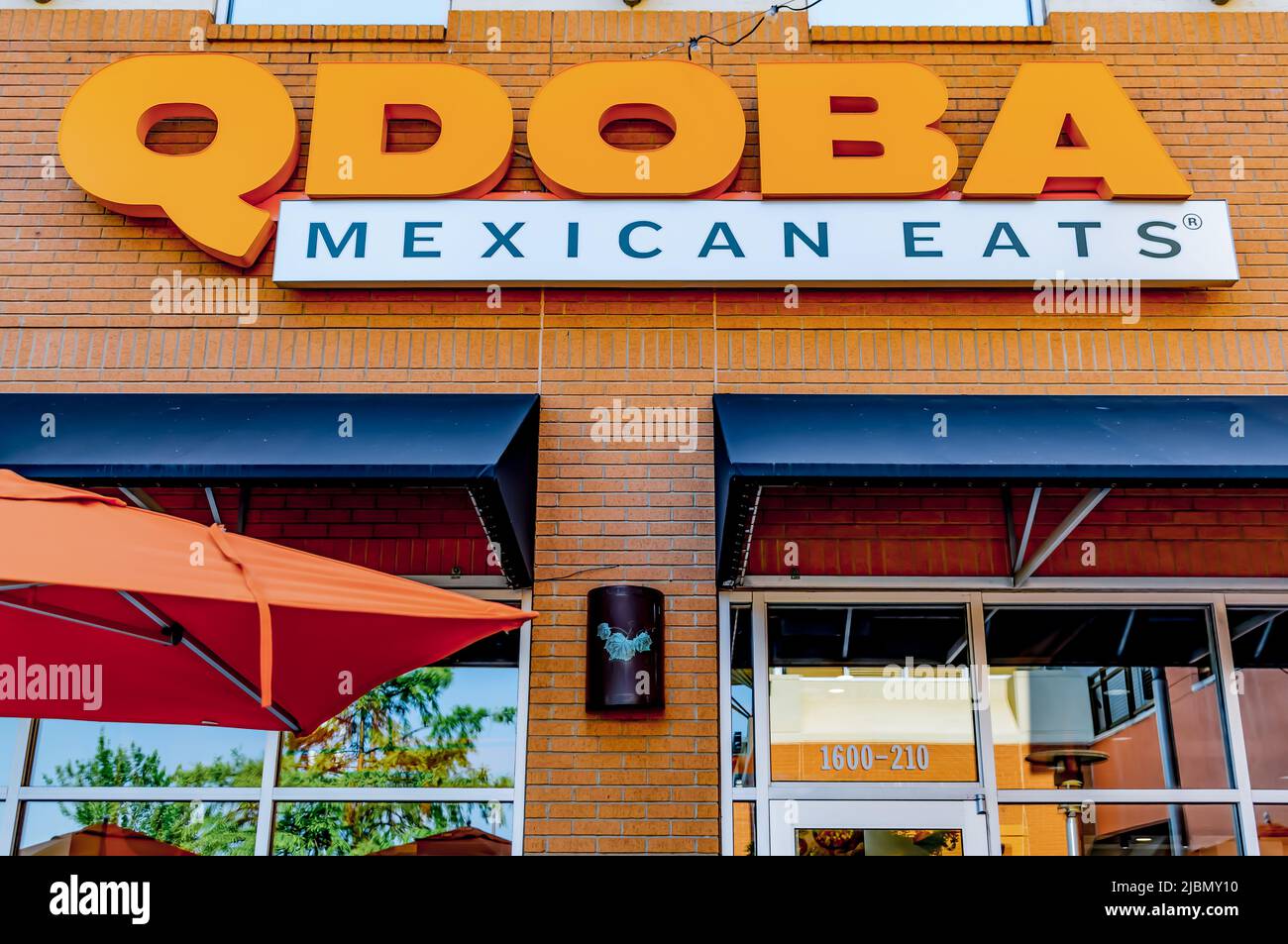 Qdoba Mexican isst die Außenfassade des Restaurants mit orangefarbenen Buchstaben über schwarzen Markisen, Glasfenstern und orangefarbenem Regenschirm. Stockfoto
