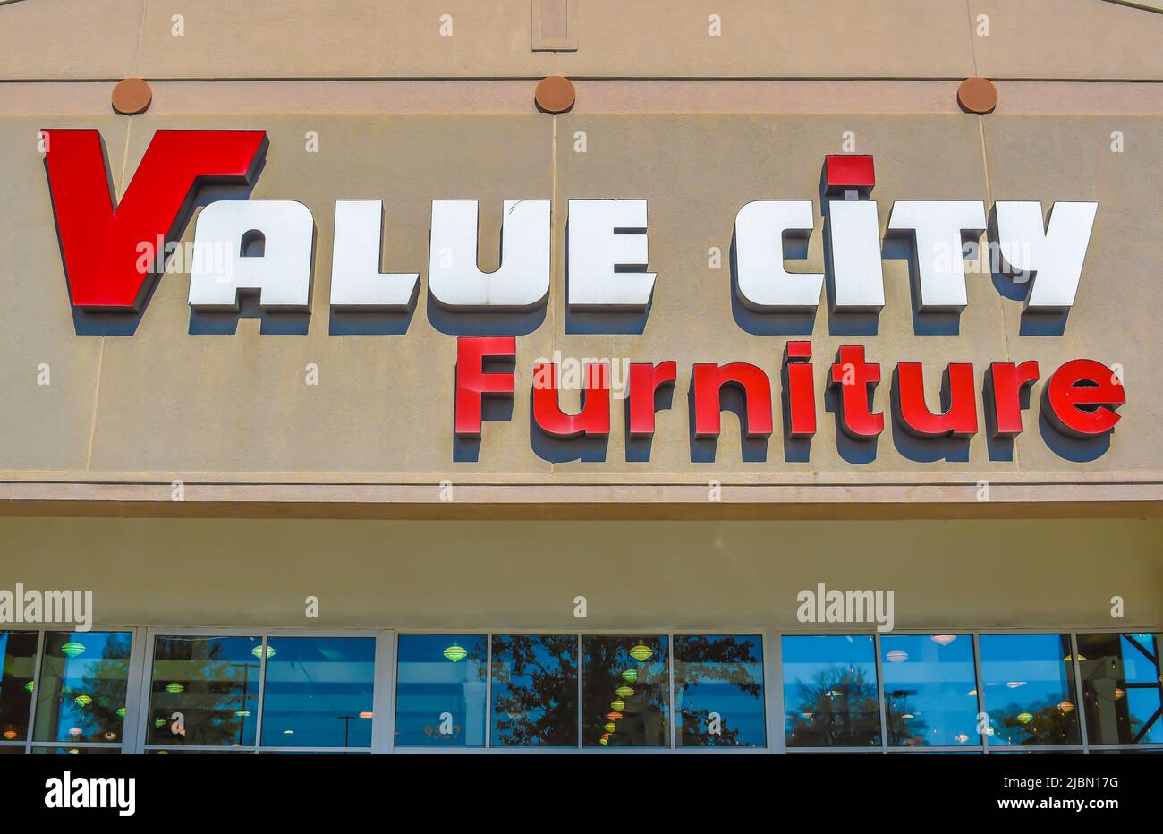 An einem sonnigen Tag über reflektierenden Glasfenstern sind die Außenfassade des Möbelhauses Value City und das Logo in roten und weißen Buchstaben gekennzeichnet. Stockfoto