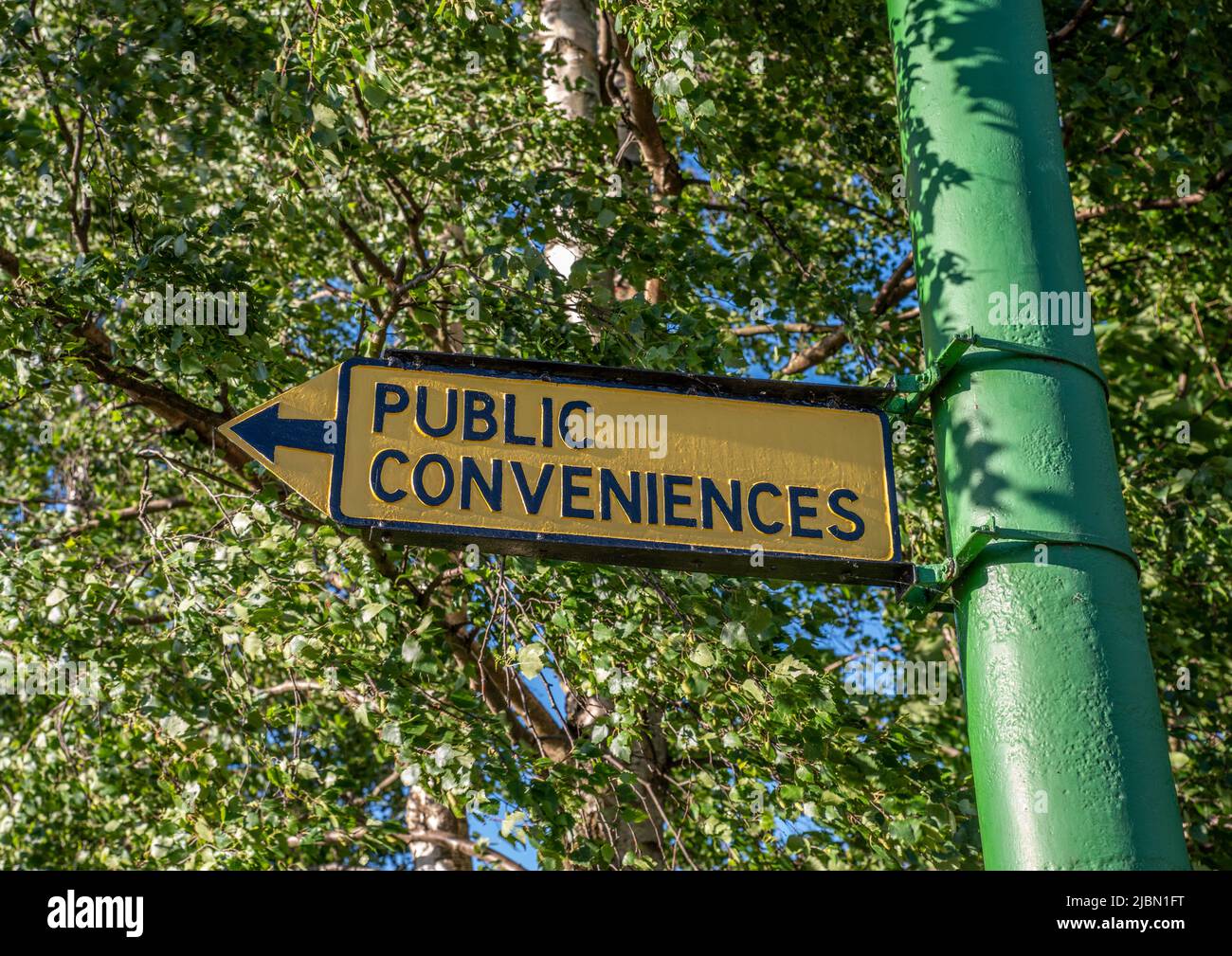 Vintage schwarz und gelb Public Convenience-Schild mit einem Pfeil auf einem grünen Pfosten. Stockfoto