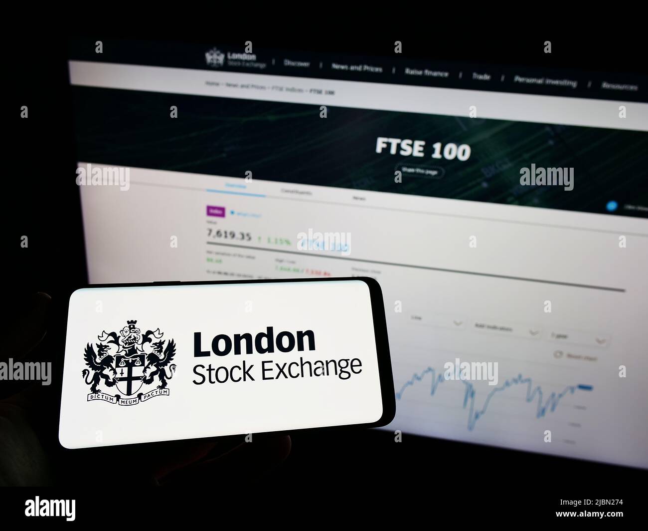 Person mit Mobiltelefon und Logo des Finanzmarktplatzes London Stock Exchange (LSE) auf dem Bildschirm vor der Webseite. Konzentrieren Sie sich auf die Telefonanzeige. Stockfoto