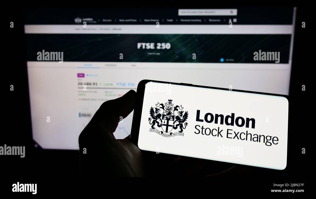 Person mit Mobiltelefon und Logo des britischen Marktplatzes London Stock Exchange (LSE) auf dem Bildschirm vor der Webseite. Konzentrieren Sie sich auf die Telefonanzeige. Stockfoto