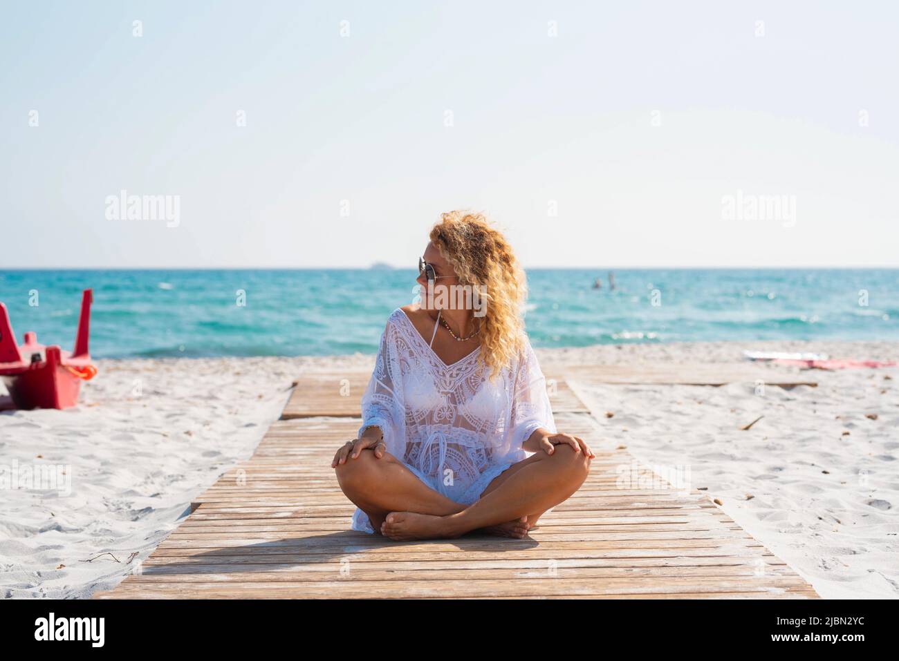 Weibliche genießen Sonne und Bräune am Strand in Sommerurlaub Urlaub Freizeit-Aktivität. Eine Frau sitzt auf einem hölzernen Pier auf dem Sand mit Blau Stockfoto Weibliche genießen Sonne und Bräune am Strand in Sommerurlaub Urlaub Freizeit-Aktivität. Eine Frau sitzt auf einem hölzernen Pier auf dem Sand mit Blau Stockfoto