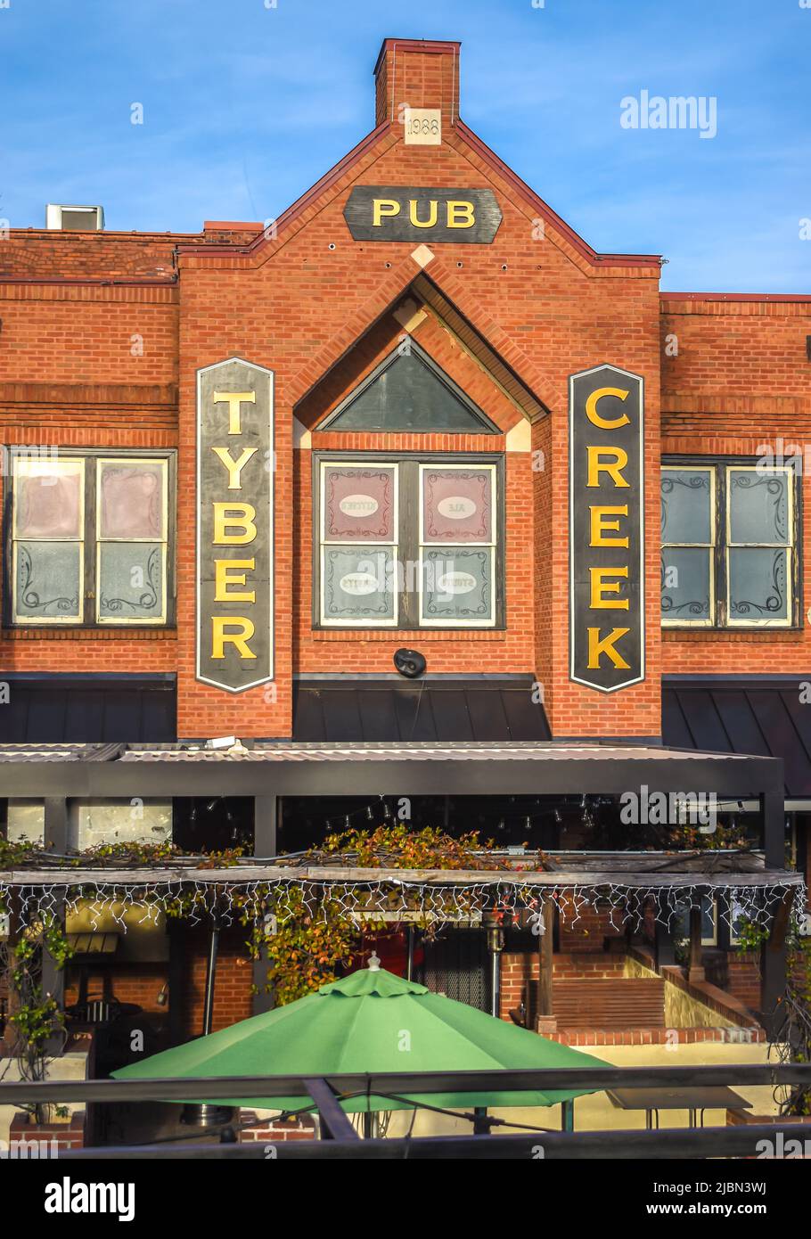 Tyber Creek Pub's Außenfassade Marke und Logo Signage mit blauem Himmel, reflektierenden Glasfenstern, Terrasse und grünem Regenschirm in Charlotte, NC. Stockfoto