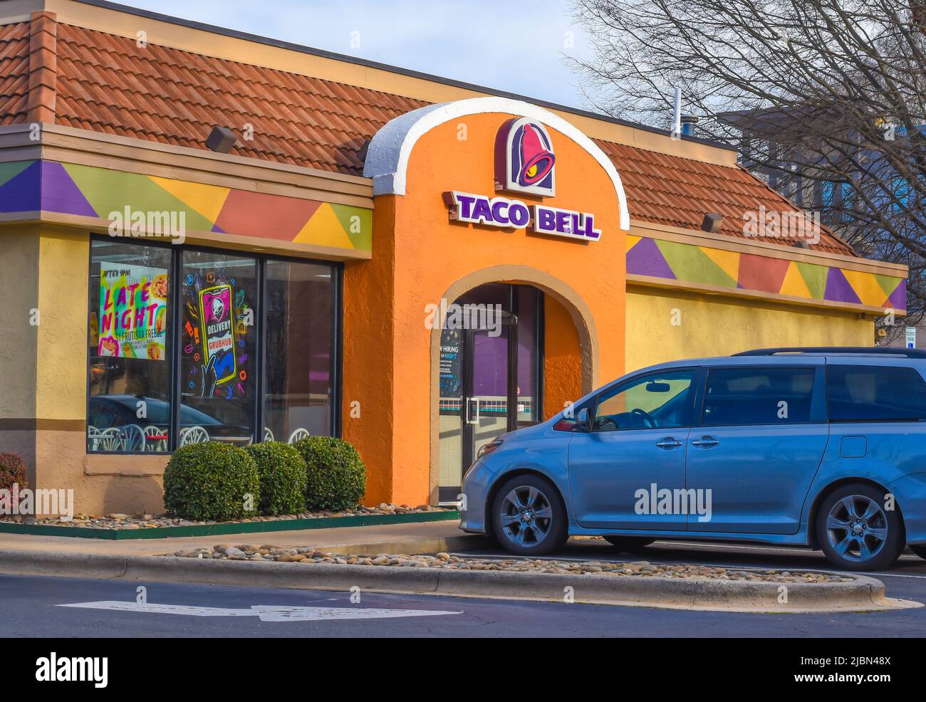 Taco Bell's Außenfassade Marke und Logo Signage in lila Buchstaben auf adobe tan Eingangsfassade mit Himmel und nackten Ästen von Bäumen in Charlotte. Stockfoto