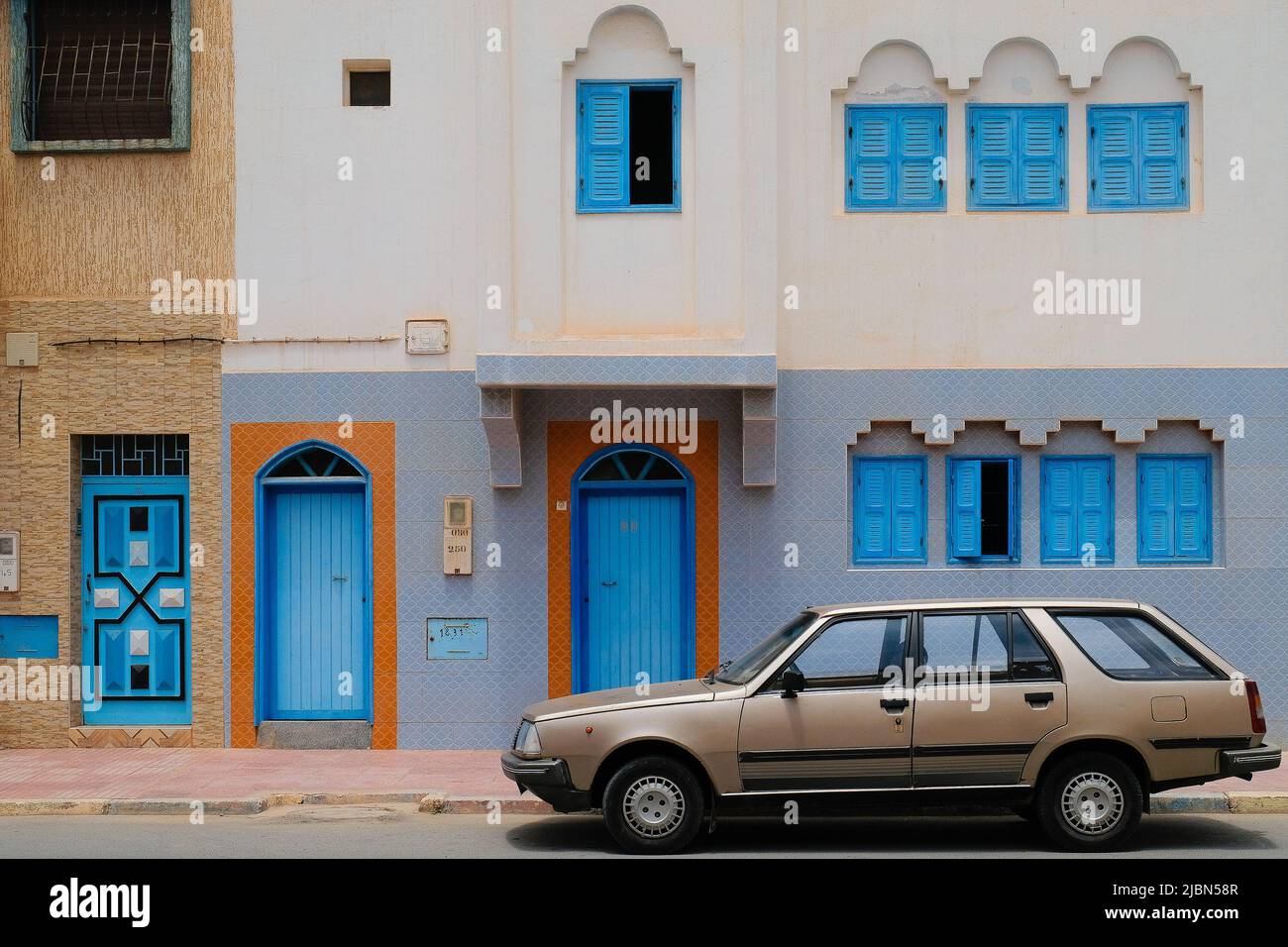 Sidi Ifni, Marokko: Oldtimer-Kombi, der vor einem Gebäude mit bunten Türen und Fenstern in einer Mischung aus marokkanischem und spanischem Design geparkt ist. Stockfoto