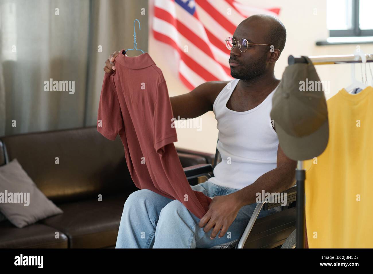 Afroamerikanischer Mann sitzt im Rollstuhl und wählt T-Shirt für einen Tag Stockfoto