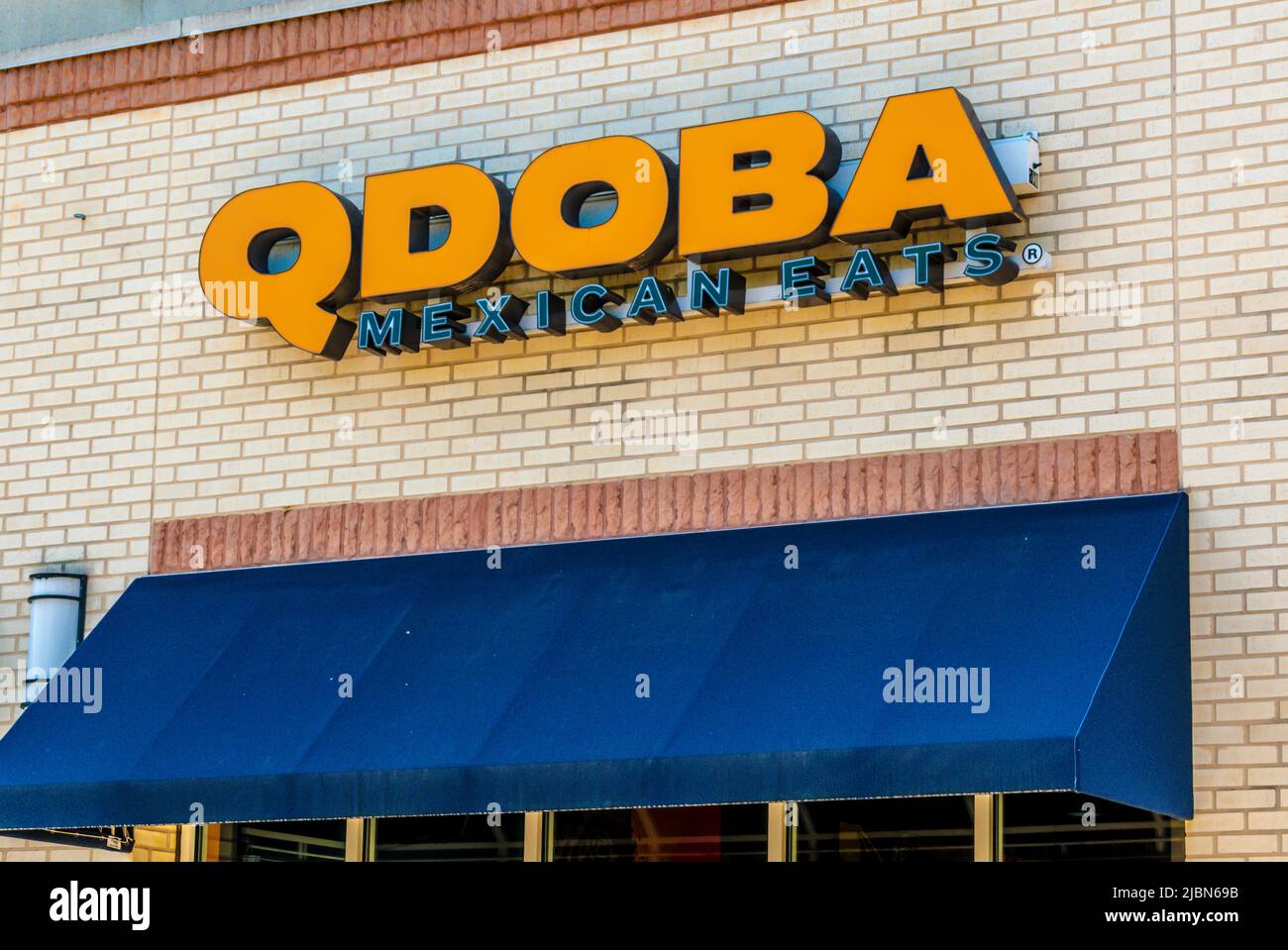 Qdoba Mexican isst an einem sonnigen Tag eine Außenfassade mit orangefarbenen Buchstaben auf beigefarbenen Ziegeln über einer blauen Markise. Stockfoto