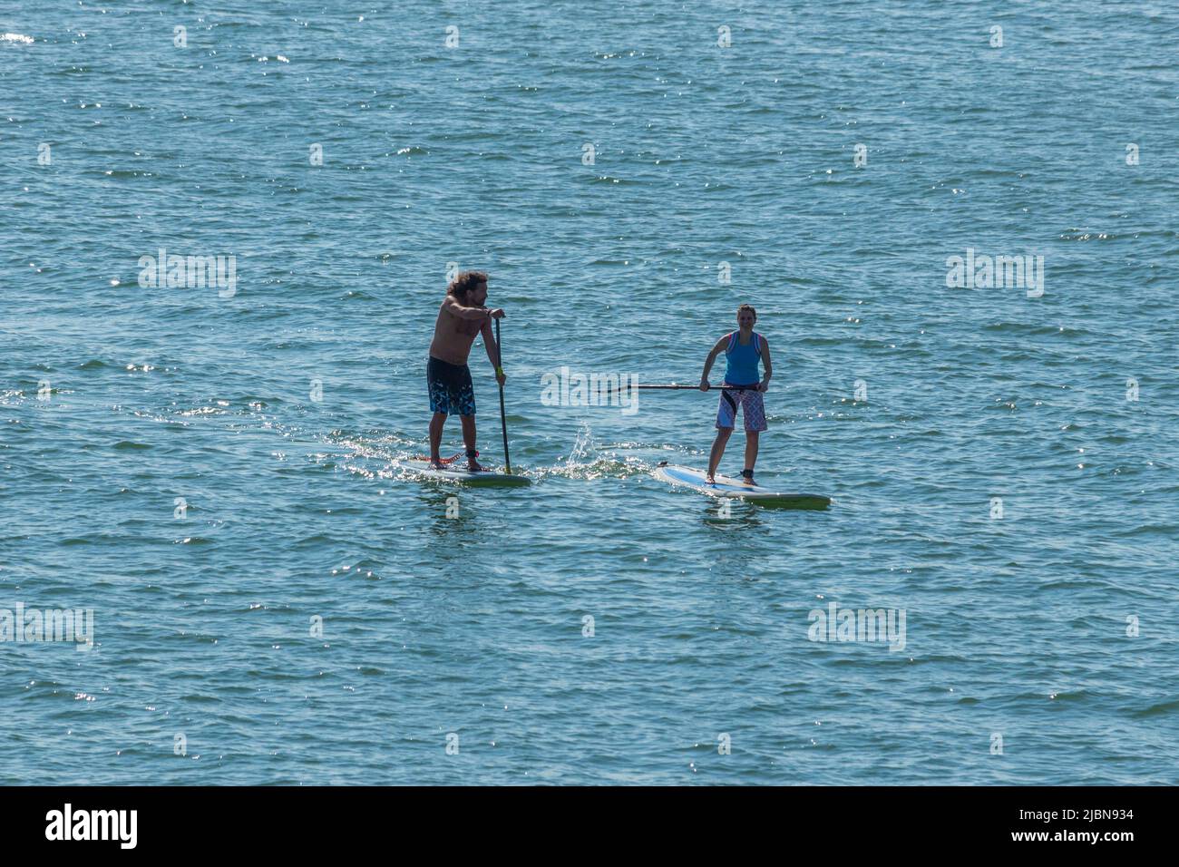 Zwei unbekannte Personen, ein Mann und eine Frau paddeln im Meer. Aufgenommen in Hastings, Großbritannien im Englischen Kanal. Stockfoto