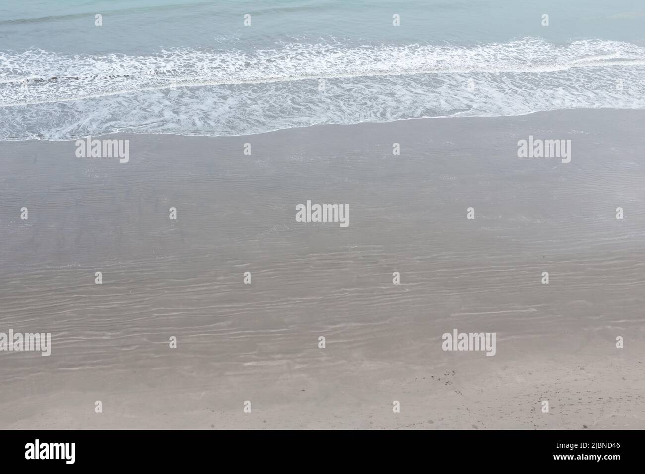 Details vom Meeresrand mit nassem Sand und Ozean mit brechenden Wellen, Hintergrund mit Natur Stockfoto