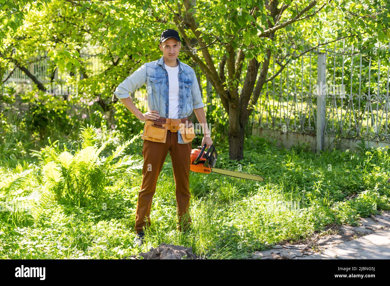 Ein Mann mit einer Kettensäge. Entfernt Pflanzungen im Garten von alten Bäumen, erntet Brennholz. Stockfoto