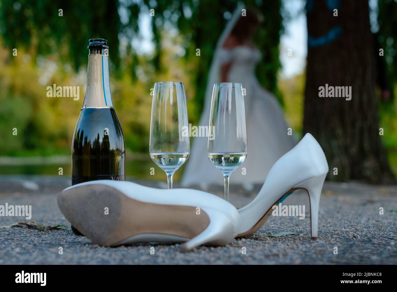 Eine Champagnerflasche, ein Paar High Heels und zwei Sektgläser befinden sich auf dem Boden im Freien, Ende einer Hochzeit Stockfoto