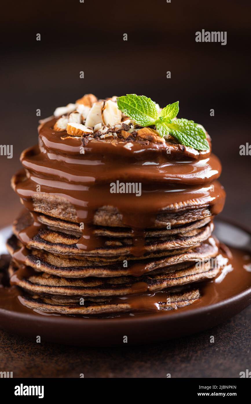 Schokoladenpfannkuchen mit Schokoladensauce und gehackten Nüssen, Nahaufnahme, dunkler Hintergrund Stockfoto